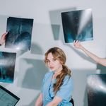 A female healthcare worker in blue scrubs reviews multiple X-ray images indoors.